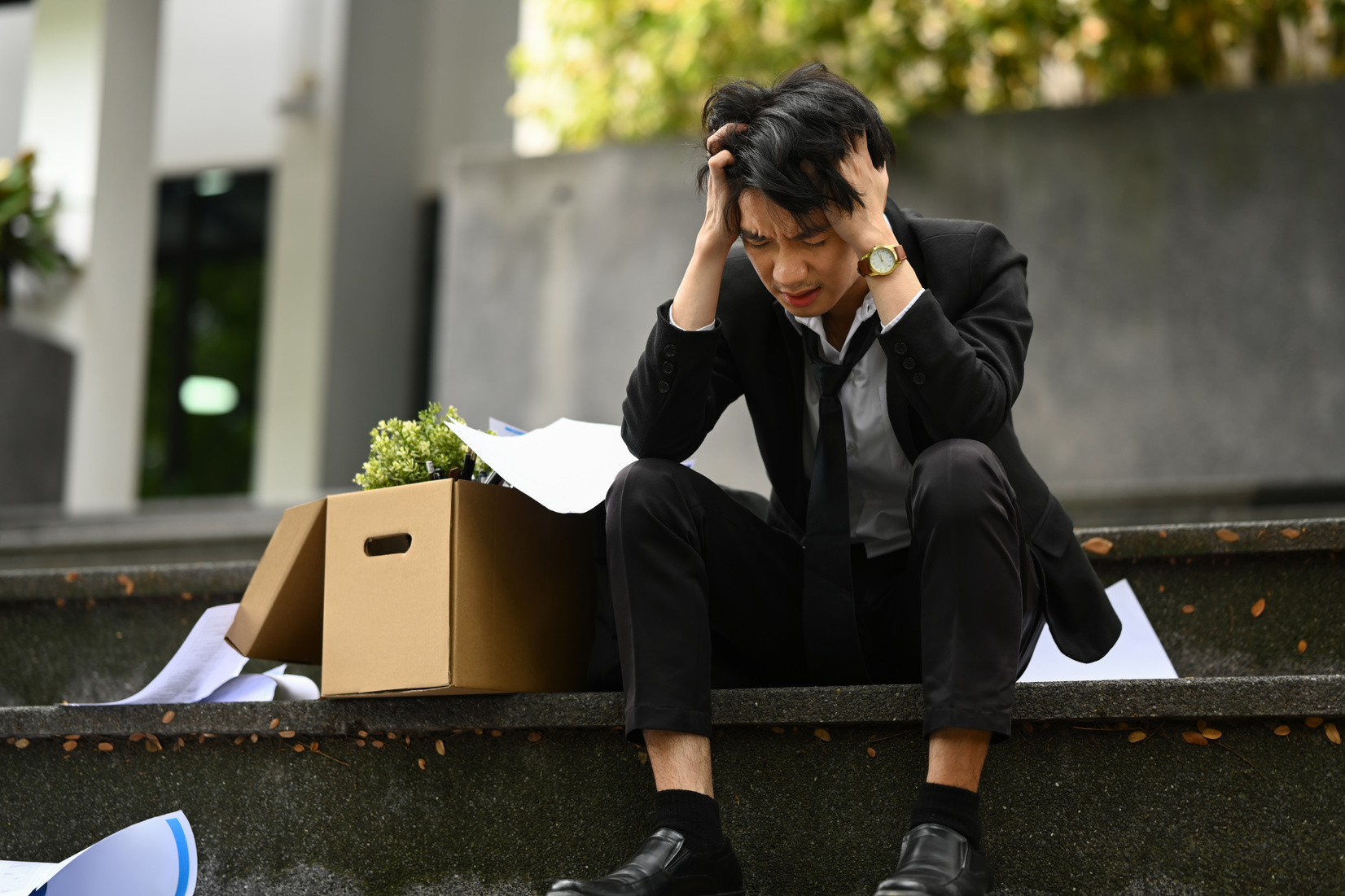 Upset businessman sitting hopelessly on stairs of building with box of personal stuff. Unemployed, depressed and financial crisis